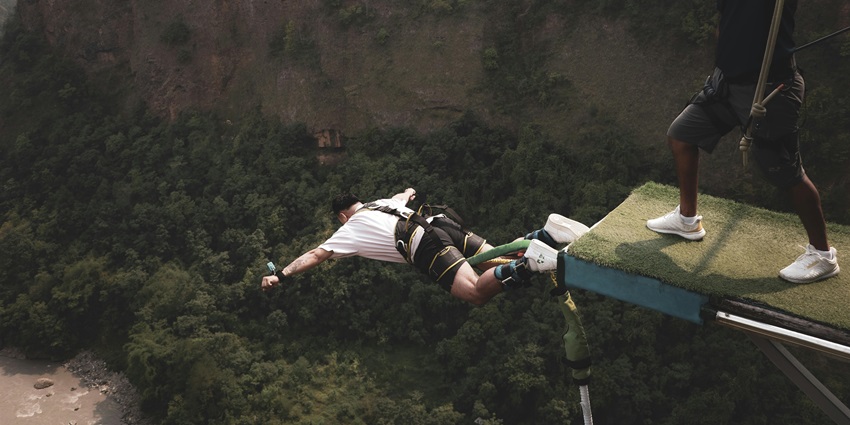 Man at the popular bungee jumping location in Pokhara over a river surrounded by lush greenery and water below.