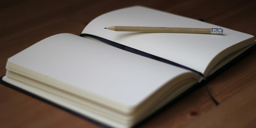 A frontal view of a white open notebook with a pencil on top of it during the daytime.