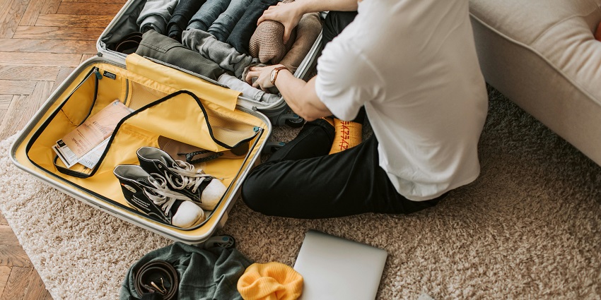 A woman on the floor with her suitcase and laptop, packing her bag before travelling.