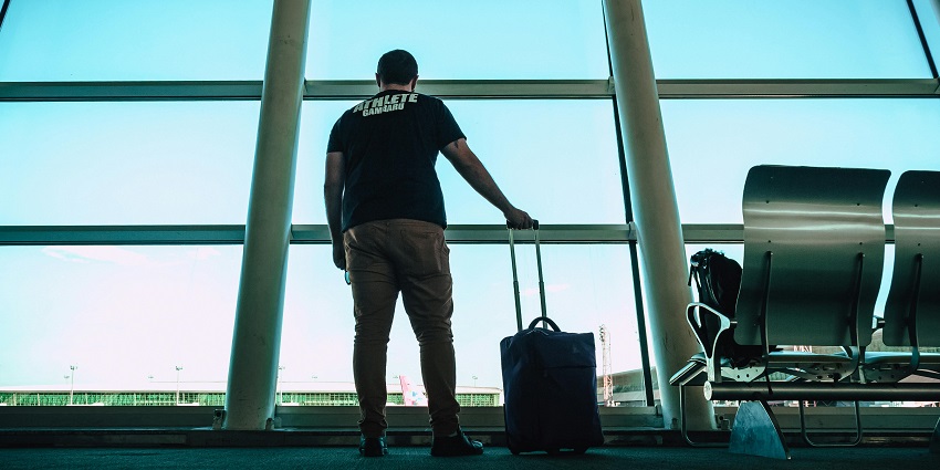 A man stands outdoors, holding a large luggage bag, ready for travel