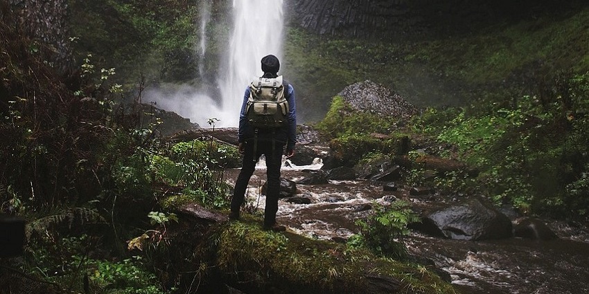 Person wearing a grey backpack and trekking around the mountains and waterfalls