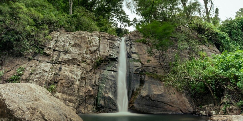 A stunning waterfall cascades down a cliff, surrounded by lush green trees