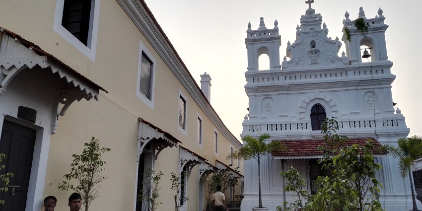 View of a church beside the Tiracol fort wall under a sunset sky