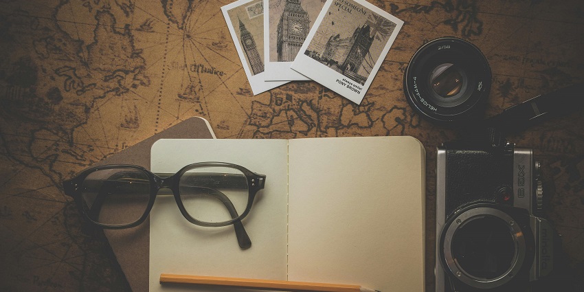An image of black-framed eyeglasses on the white book and a camera to click photos.