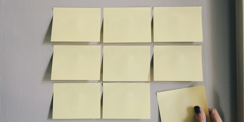 A frontal view of a plain white surface with multiple yellow sticky notes pasted on it.
