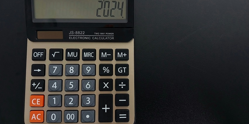 A close-up view of a grey calculator with different numbers with a black background.