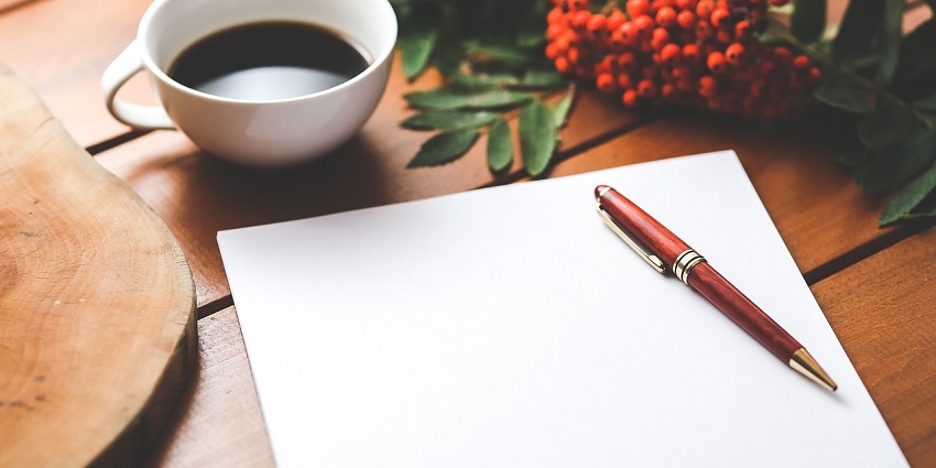 A stunning view of a white paper with a pen on it and a cup of coffee on the side.
