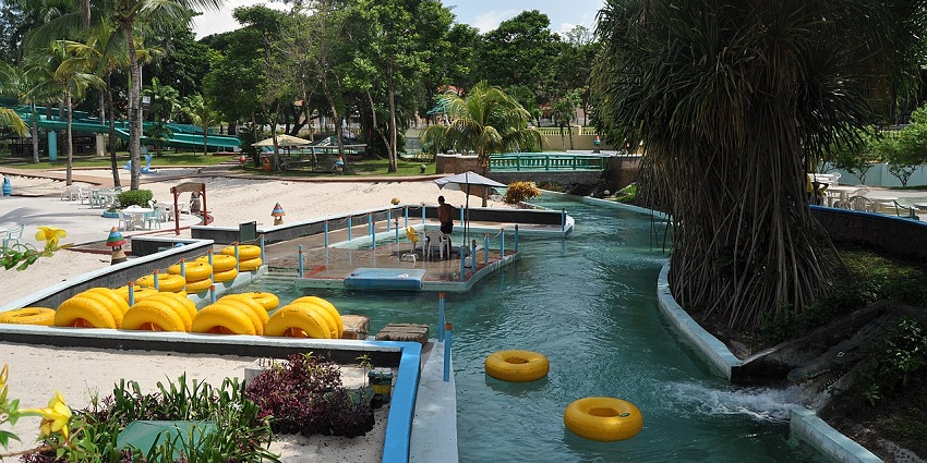 Image of water park surrounded by lush green trees and colourful play area during summer time
