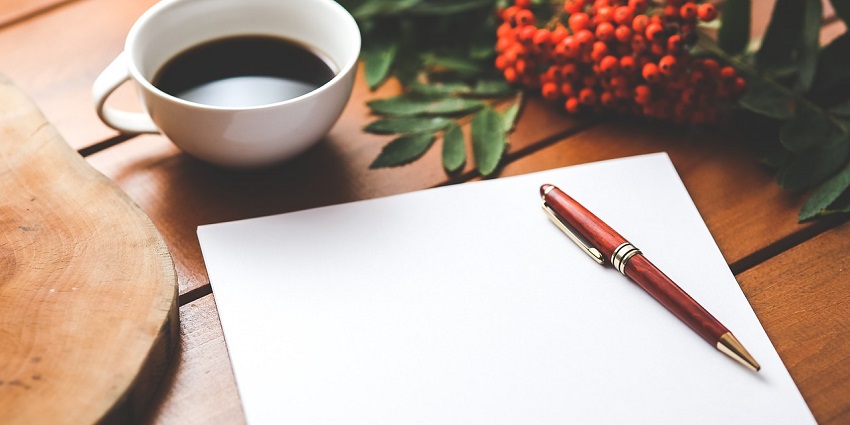 A mesmerising view of a white blank paper with a pen on top and a cup of coffee.