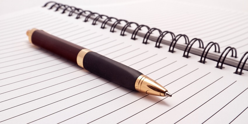 A close-up shot of a pen and paper sitting on a flat surface during the daytime.