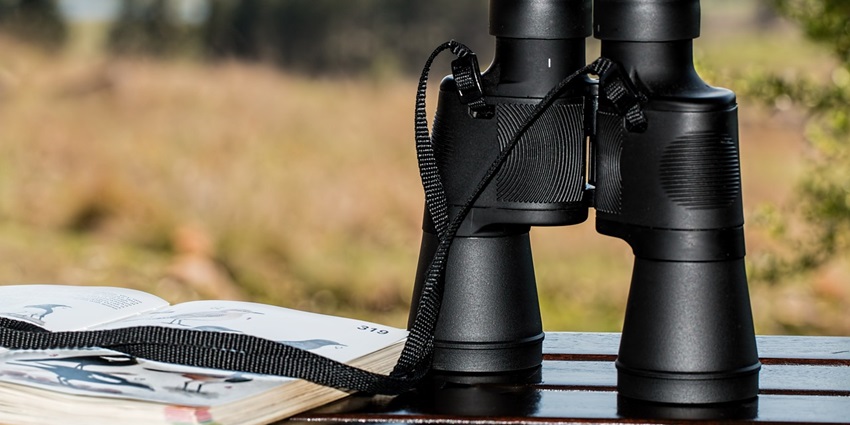 A mesmerising view of a pair of binoculars sitting on a table with an open notebook.