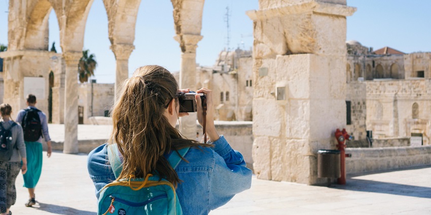 Image of a woman in blue denim wear taking pictures of fort ruins during day time
