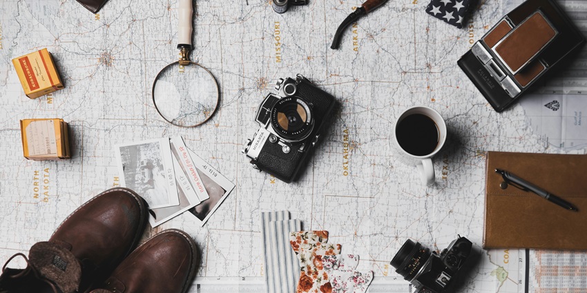 A camera, brown shoes, a white mug, a pen, and a smoking pipe arranged on a table.