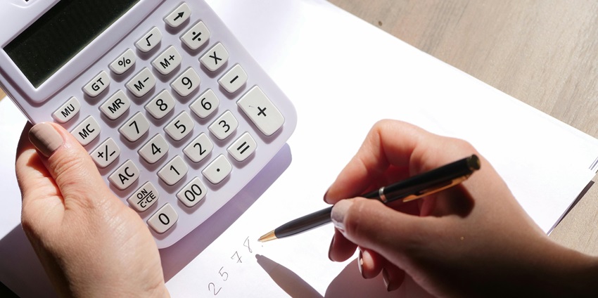 An aerial shot of a person using a white calculator and writing on paper with a black pen.