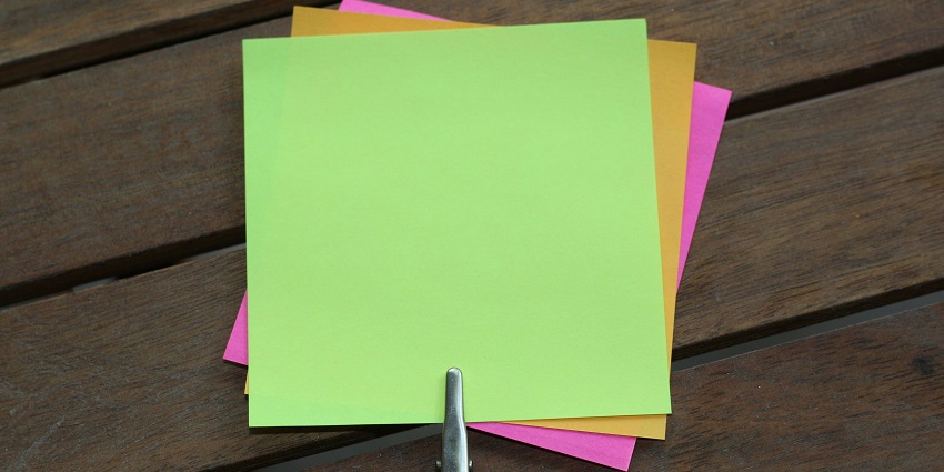 A view of a pile of colourful small pieces of paper on a brown table with a pen on it.