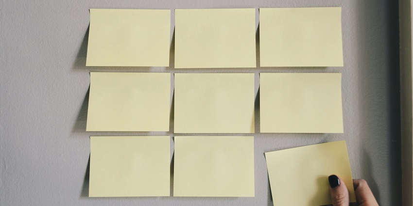 A frontal view of six different yellow sticky notes pasted on a plain white wall.