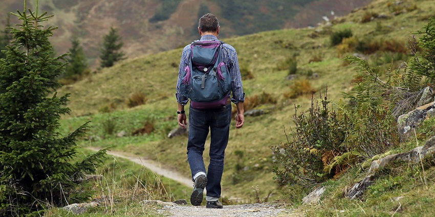 Image of man walking through lush green hills with a backpack under clear blue sky
