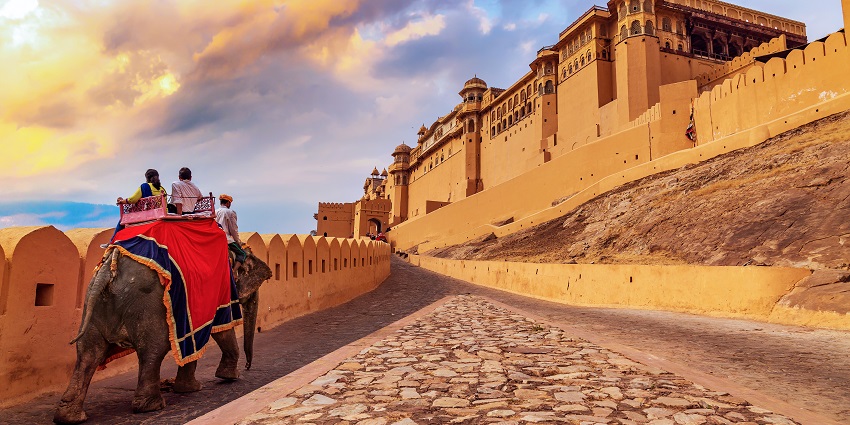 A person riding an elephant in the corridor of an ancient fort in Udaipur during sunset.