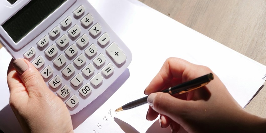 A selectively focused view of a person’s hand with a black pen and white calculator.