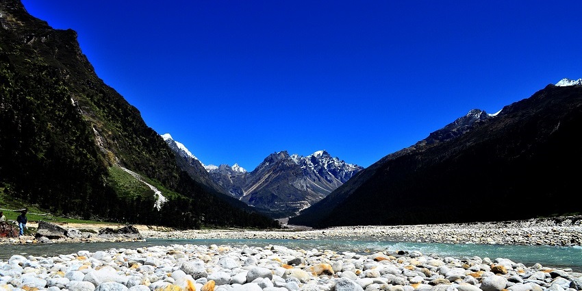 Rocky shores of a crystal clear river streaming through the verdant meadows of the valley
