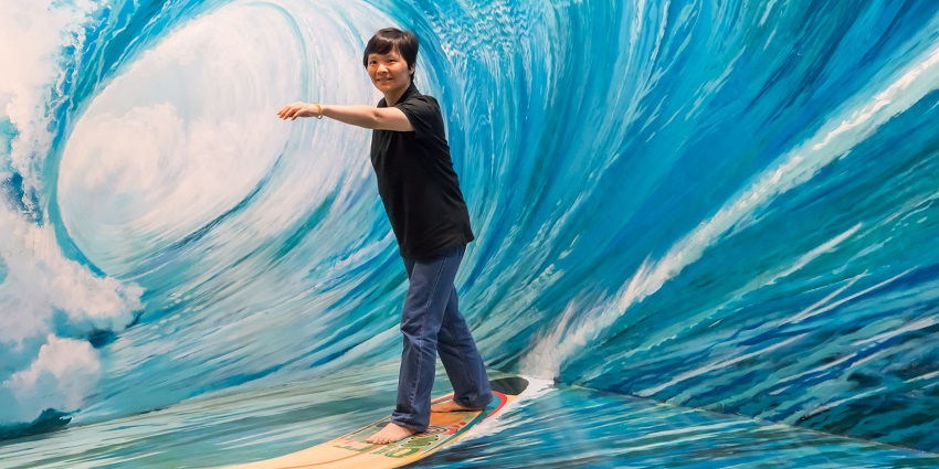 A visitor posing on the surfing illusion embedded in the wall, making it look like they're surfing