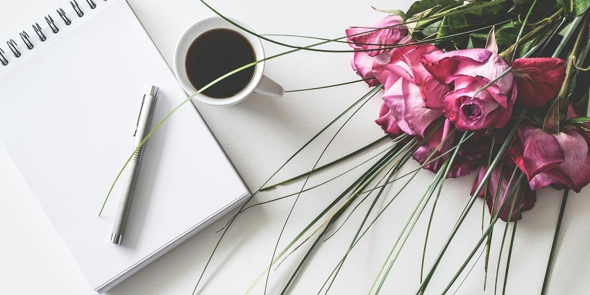 A stunning aerial shot of a notebook with a pen on it and a cup of coffee on the side.
