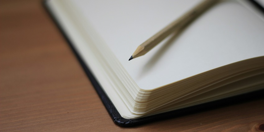 A stunning shallow focused view of a notebook with a yellow pencil sitting in it.