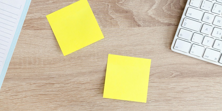 An aerial photograph of two yellow sticky notes on a table with a keyboard on the side.