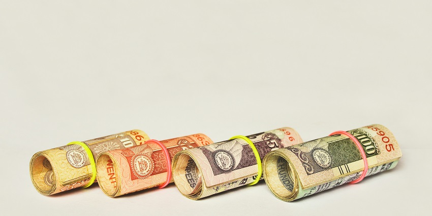 A selectively focused view of four rupee notes tied in rubber bands sitting on a table.