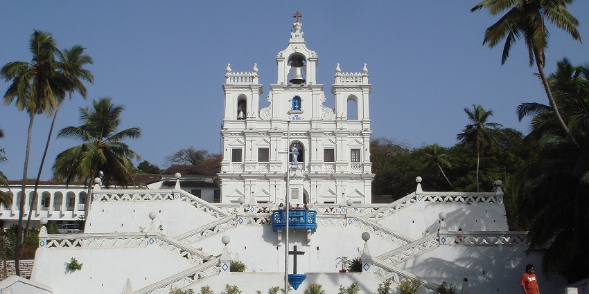 A grand colonial-era church with a pristine white facade, zigzagging staircase and towering bell.
