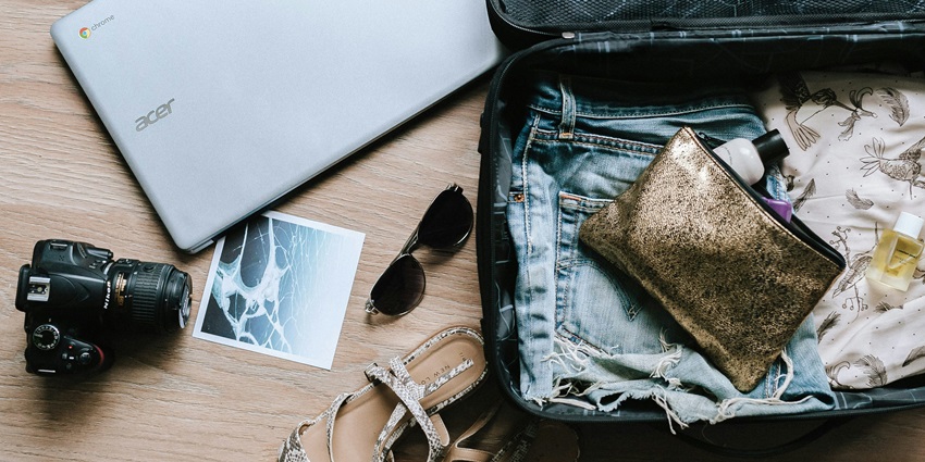 Black DSLR camera placed beside sunglasses and a brown bag on a wooden surface.