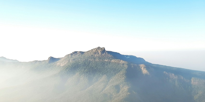 A breathtaking view of a lush green hill range under heavy fog during the daytime.