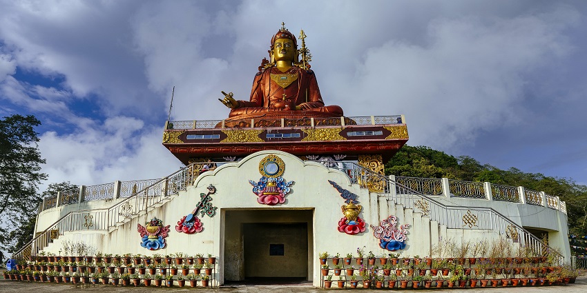 A frontal view of a tall statue of a Buddhist deity perched on top of a Monastery