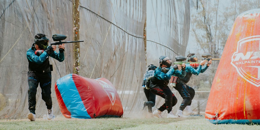 Excited players in action at a paintball game, wearing helmets and targeting their rivals.