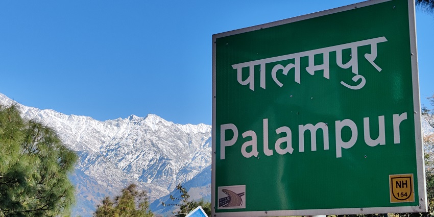 Image of Palampur hill station with a sign board and in background snow covered mountains