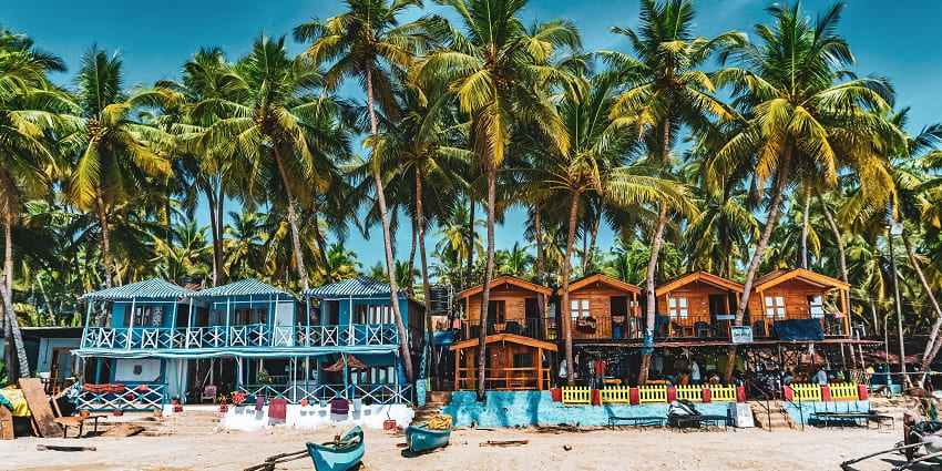 An astonishing view of colourful wooden houses in front of tall swaying palm trees.