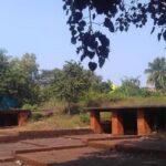 A scenic view of brick buildings set in a lush field, showcasing the Panchu Pandav Caves in Odisha.