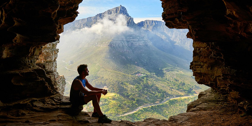 Image of a man sitting on a cave and enjoying the picturesque hills view around misty weather