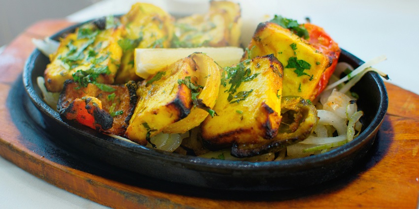 Paneer Tikka served with sliced onions, bell peppers, and a side of green chutney is a must-try.