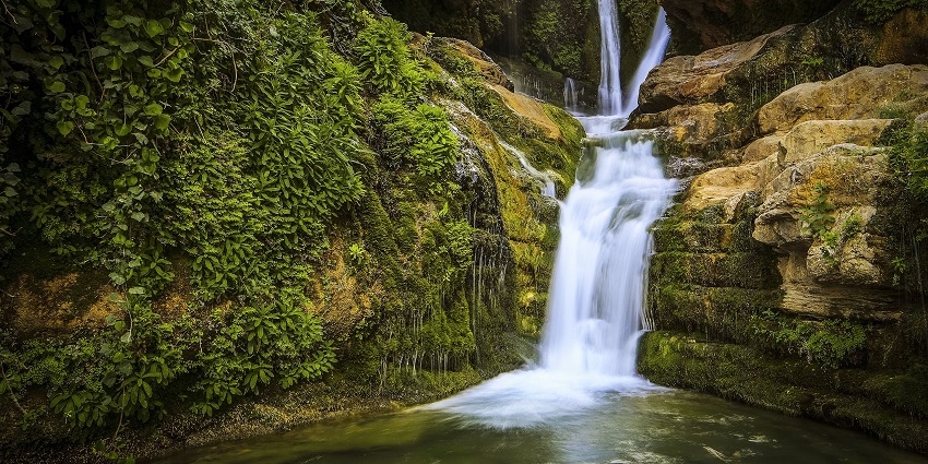 A picture of a waterfall cascading down a rocky hill and creating a big pond of water at the base