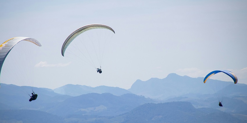 A breathtaking view of three people enjoying paragliding over lush green terrains.