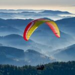 A breathtaking view of a person paragliding over a lush green valley during the daytime.