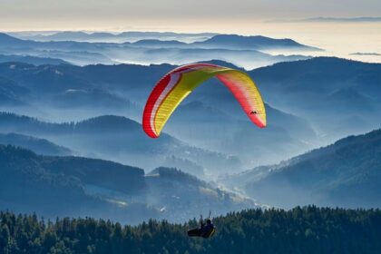 A breathtaking view of a person paragliding over a lush green valley during the daytime.