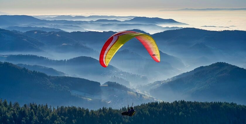 A breathtaking view of a person paragliding over a lush green valley during the daytime.