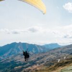 A view of a person gliding high up in the sky through majestic mountains and lush fields.