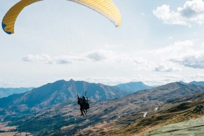 A view of a person gliding high up in the sky through majestic mountains and lush fields.