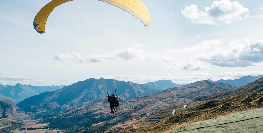 A view of a person gliding high up in the sky through majestic mountains and lush fields.