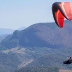 A view of a person soaring high up in the sky through majestic mountains and lush fields.