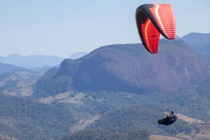 A view of a person soaring high up in the sky through majestic mountains and lush fields.