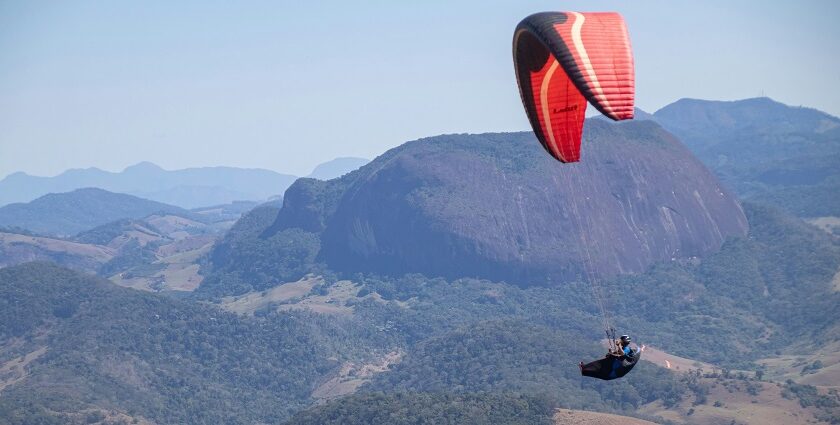 A view of a person soaring high up in the sky through majestic mountains and lush fields.